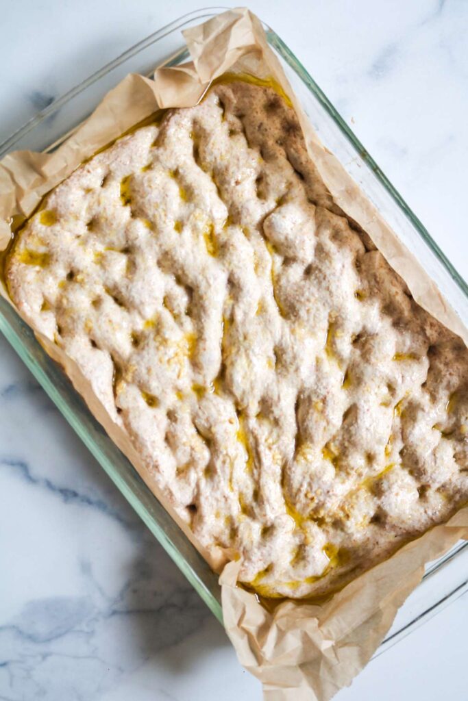 dimpled focaccia dough in glass baking dish with parchment paper